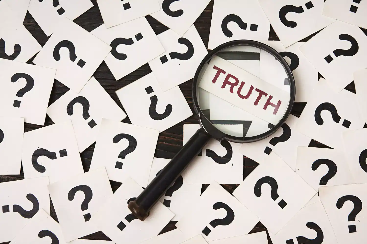 Magnifying glass revealing the word ‘TRUTH’ among scattered cards with question marks, symbolizing the search for absolute truth in a relativistic world
