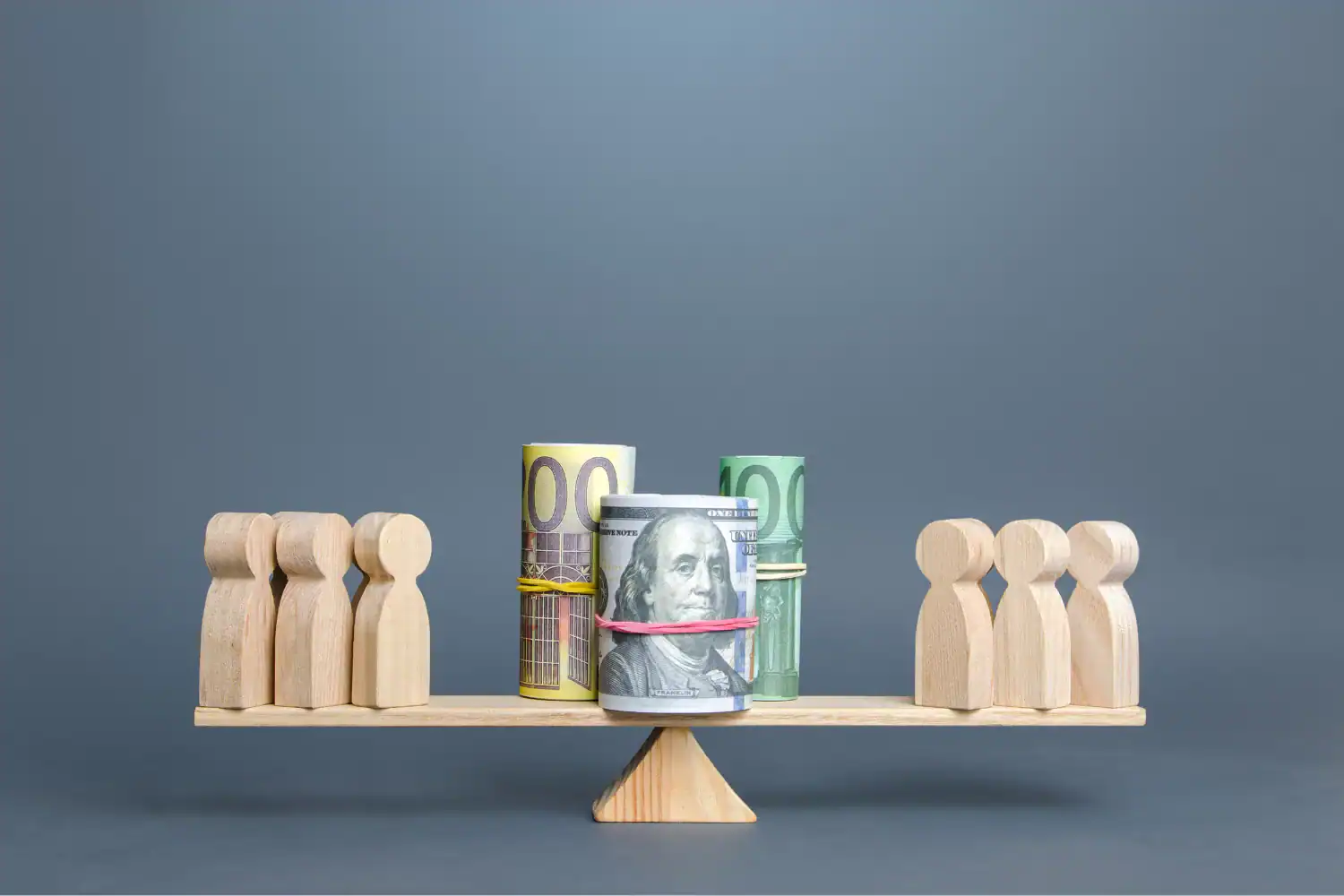 Wooden figures on a balance scale with rolled-up money in the center, symbolizing negotiating salary and fair compensation.