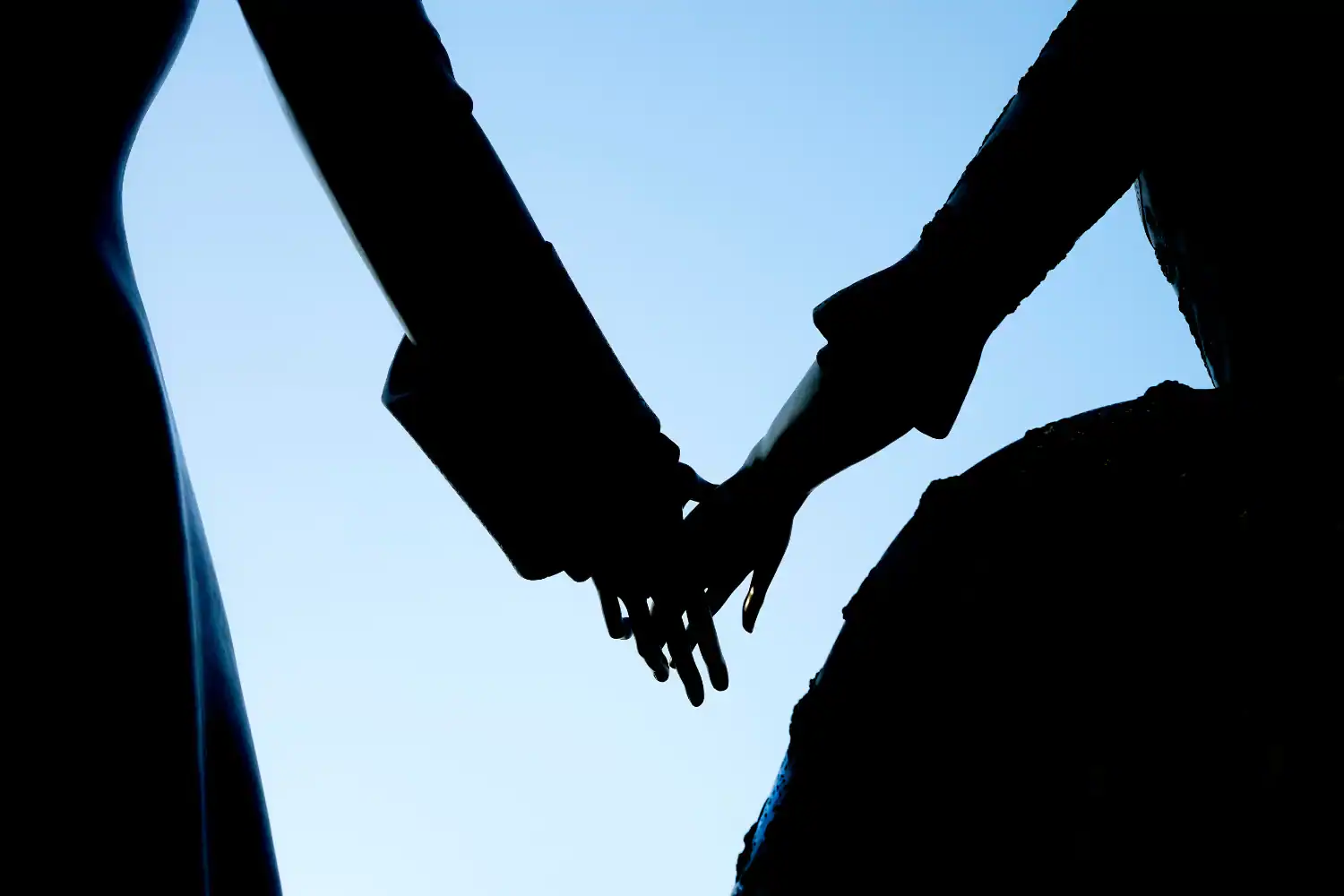 Silhouette of a man and woman holding hands against a clear sky, symbolizing the question, "what did the Puritans think about marriage?"