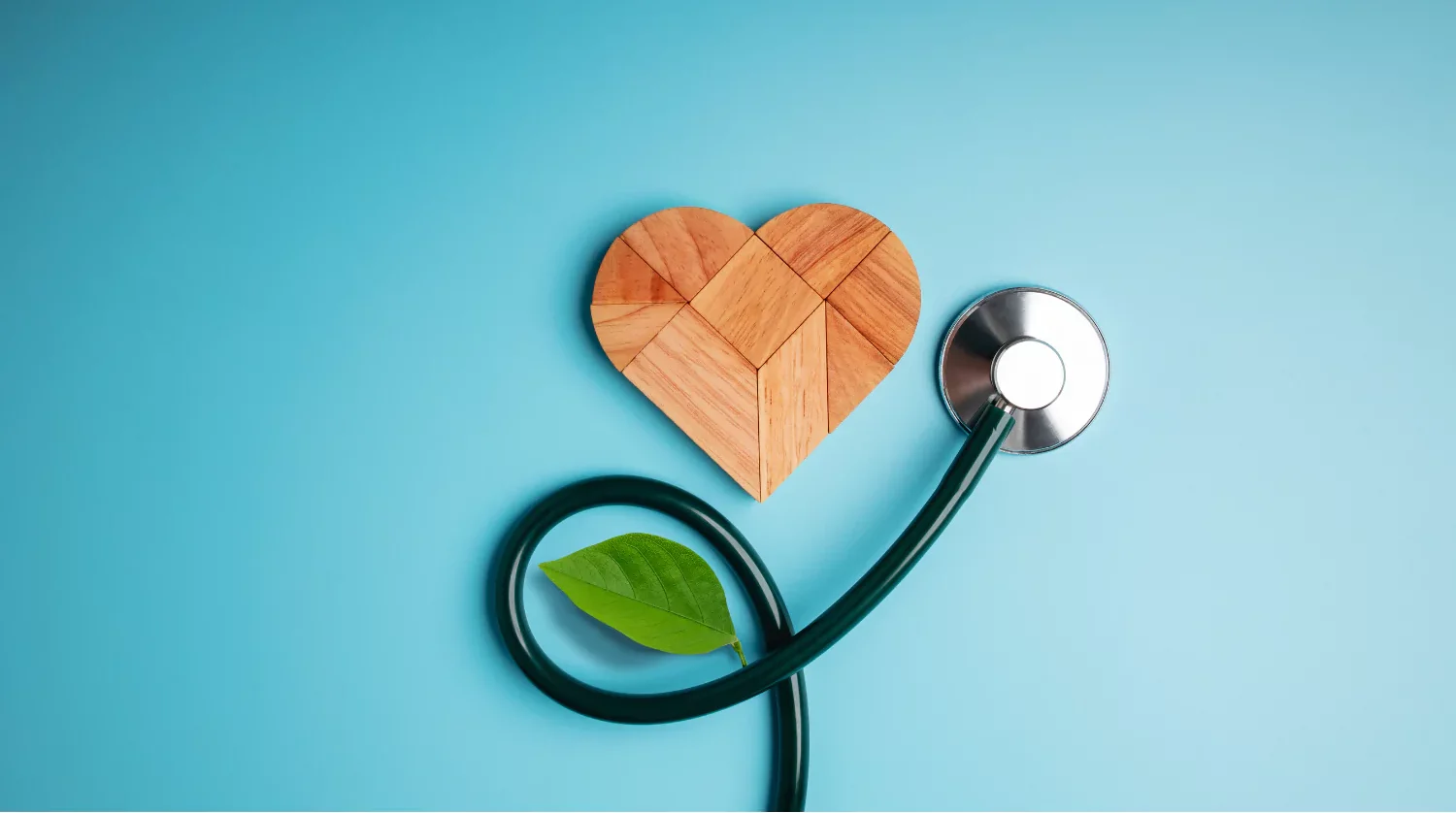 Stethoscope shaped into a heart with a wooden puzzle heart and green leaf on a blue background, symbolizing how to stay healthy.
