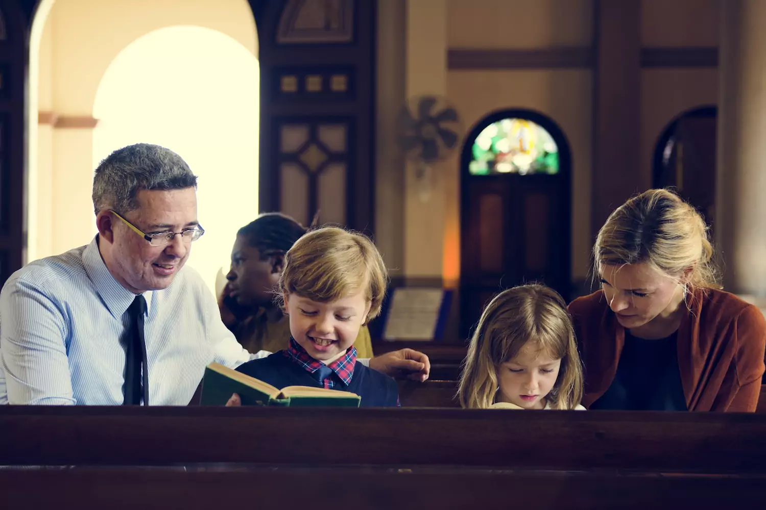 A family of four -- a dad, son, daughter and mother -- sit in a pew in a church reading hymnals.