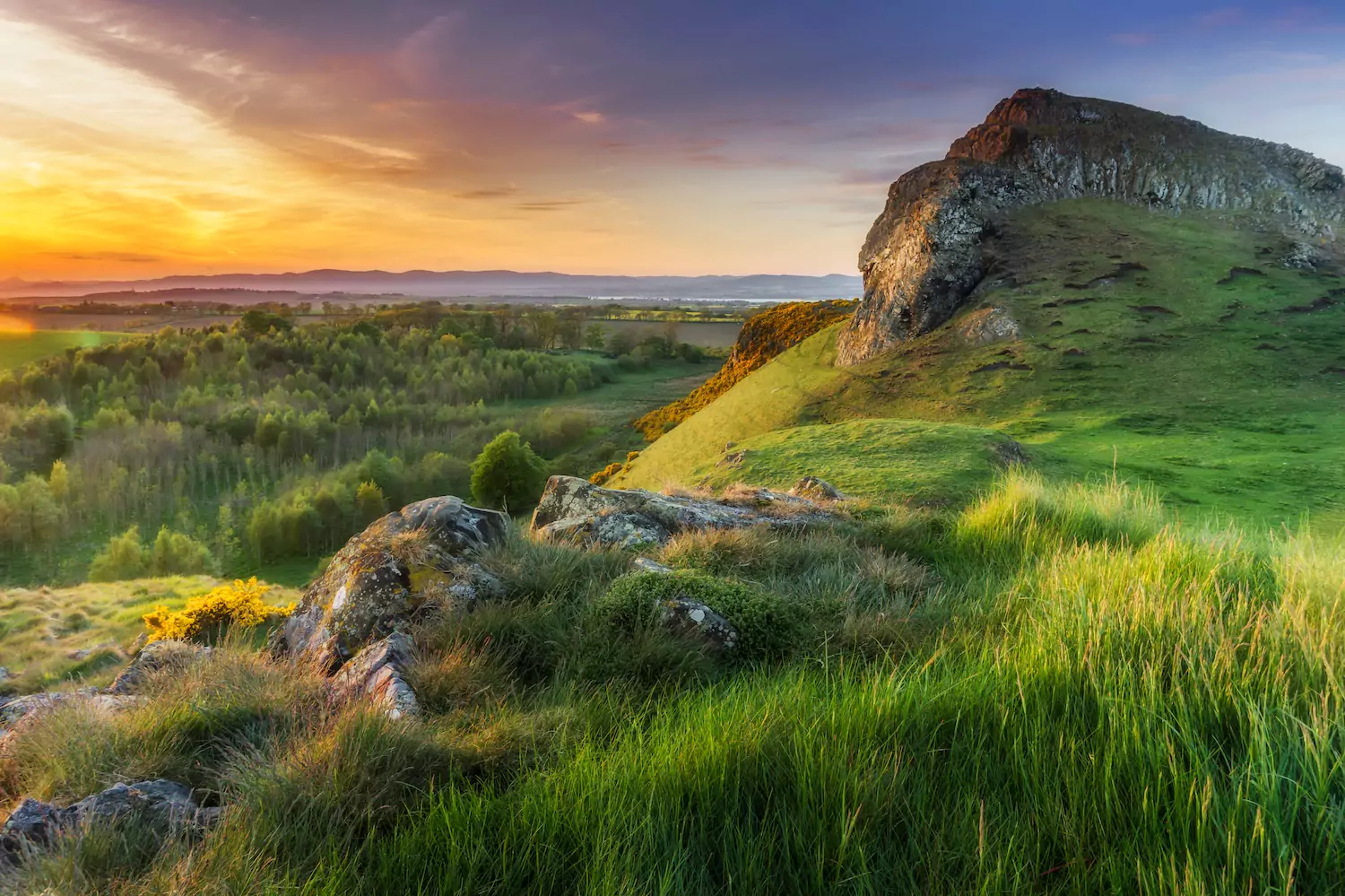 A photo of The Crags in Scotland, bathed in the light of a glorious orange sunset or sunrise.