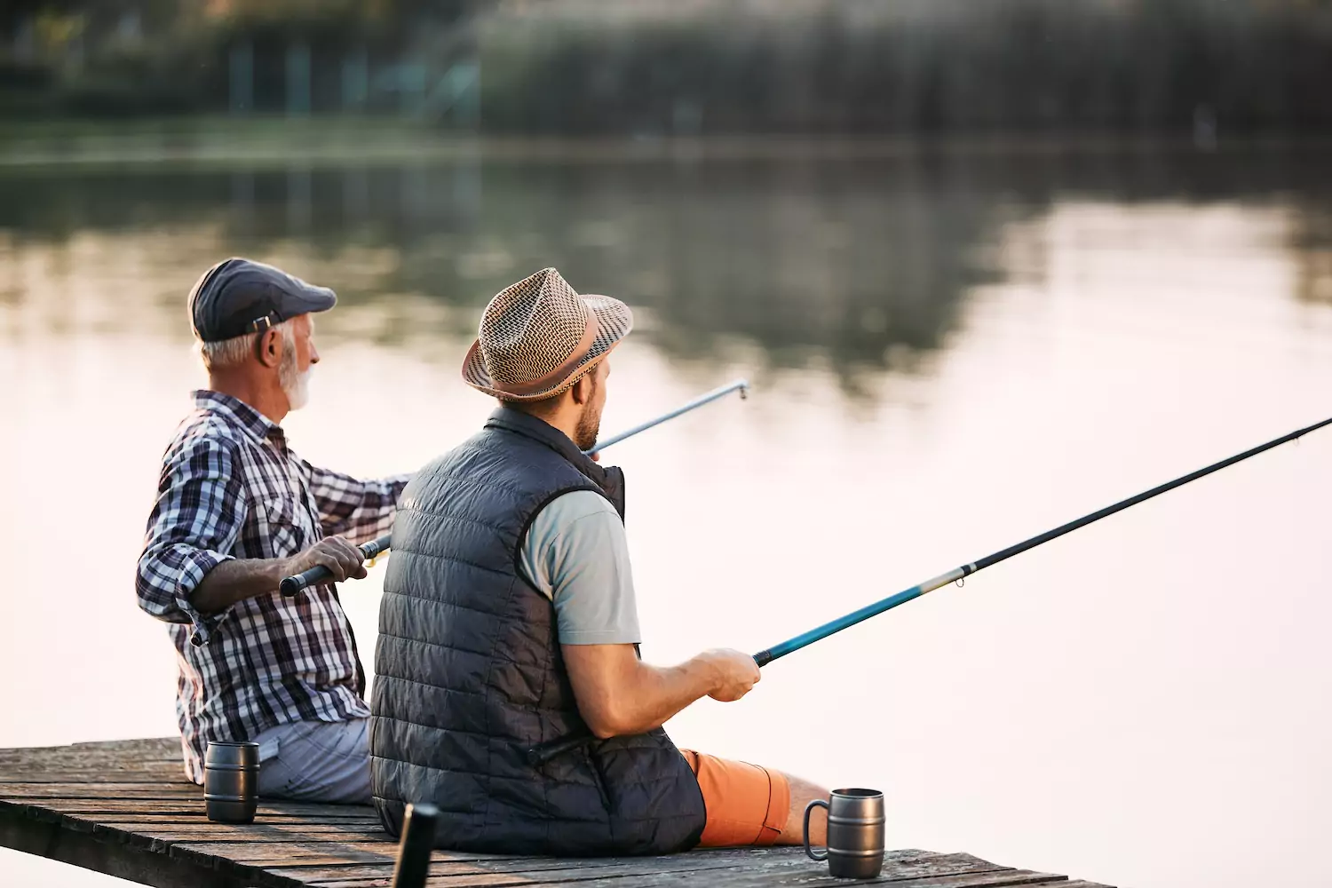 A father and a son sit on a dock, fishing together in the late afternoon light.