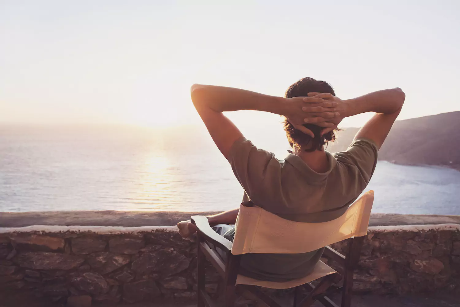 Man leaning back in a chair with his hands behind his head while looking out into the distance