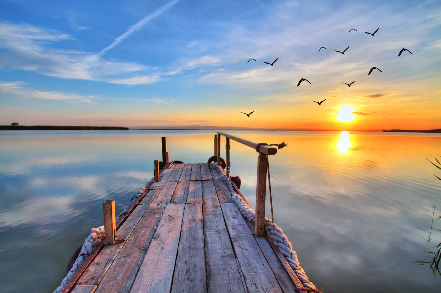 Boat dock going out into a lake with the sun in setting in the distance
