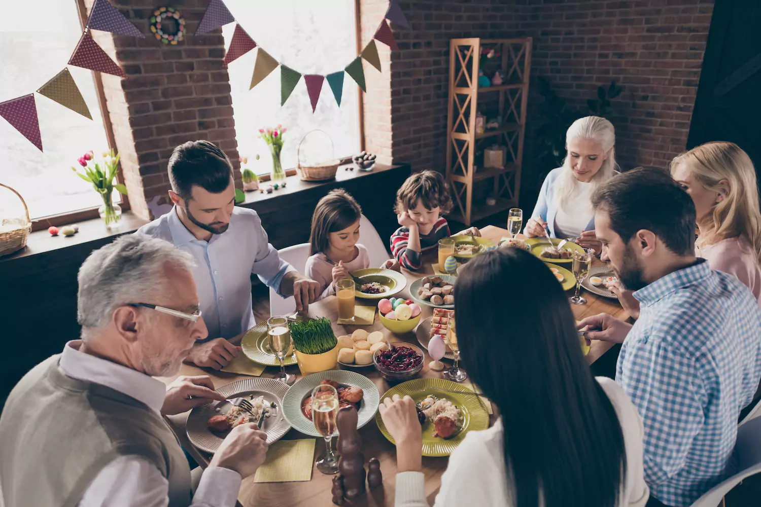 A large family sits together at a table eating their Easter meal. The home is decorated festively.