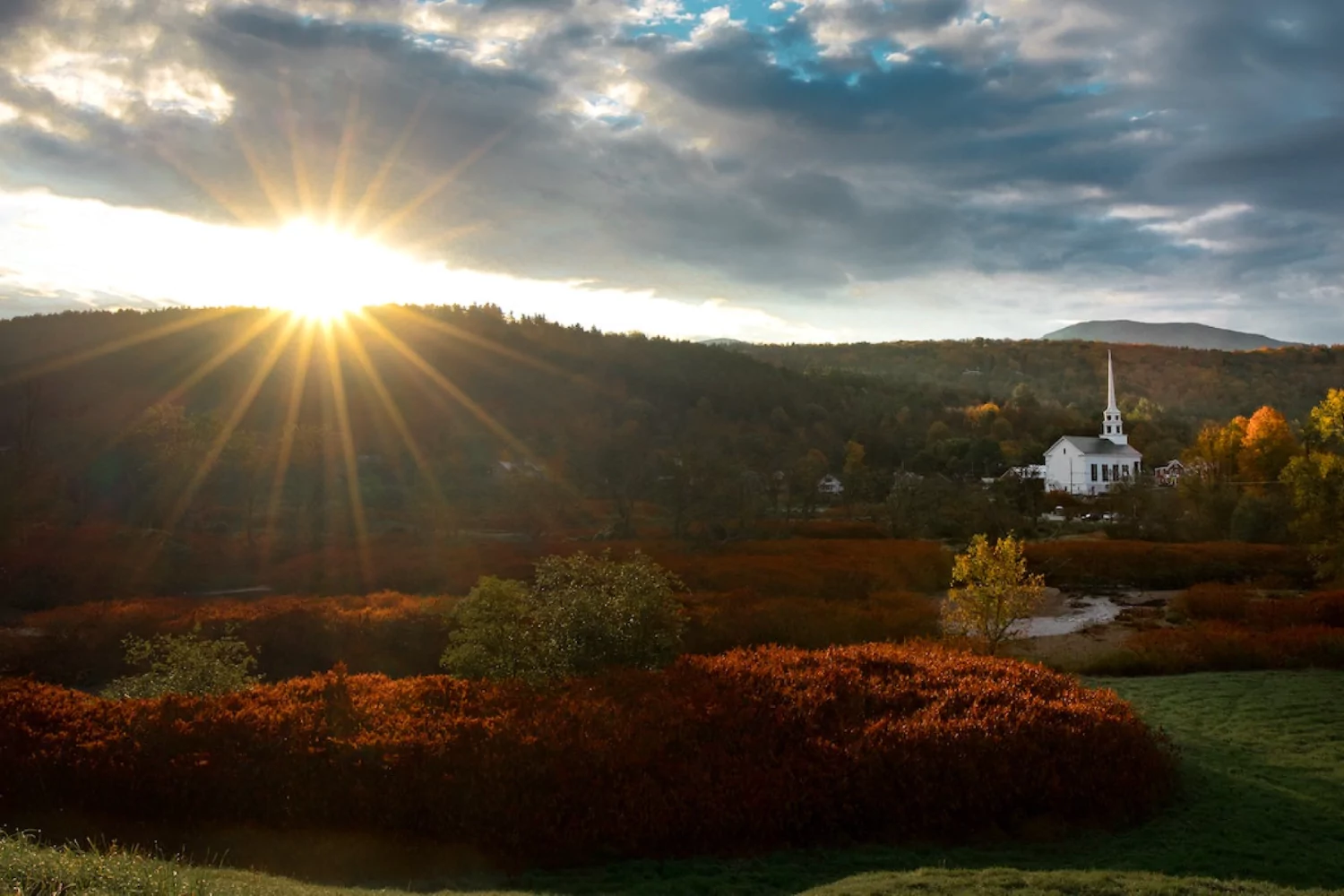 an old white church with a steeple nestled in a mountainous fall landscape