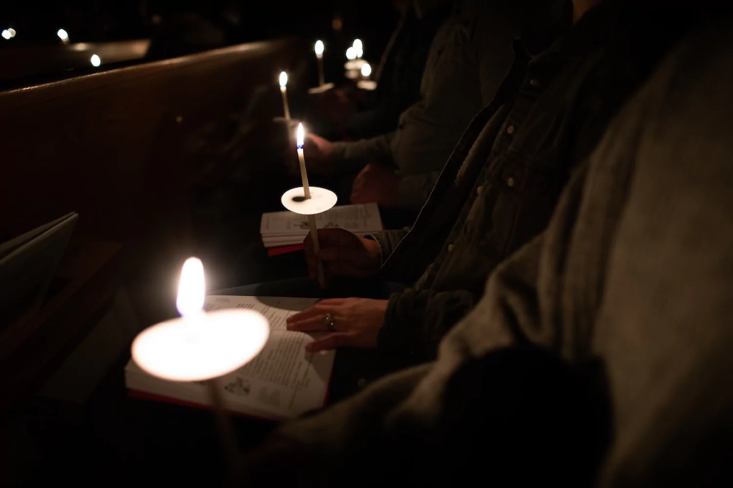 a row of worshipers at a Christmas Eve church service holding their lit candles in a dark sanctuary