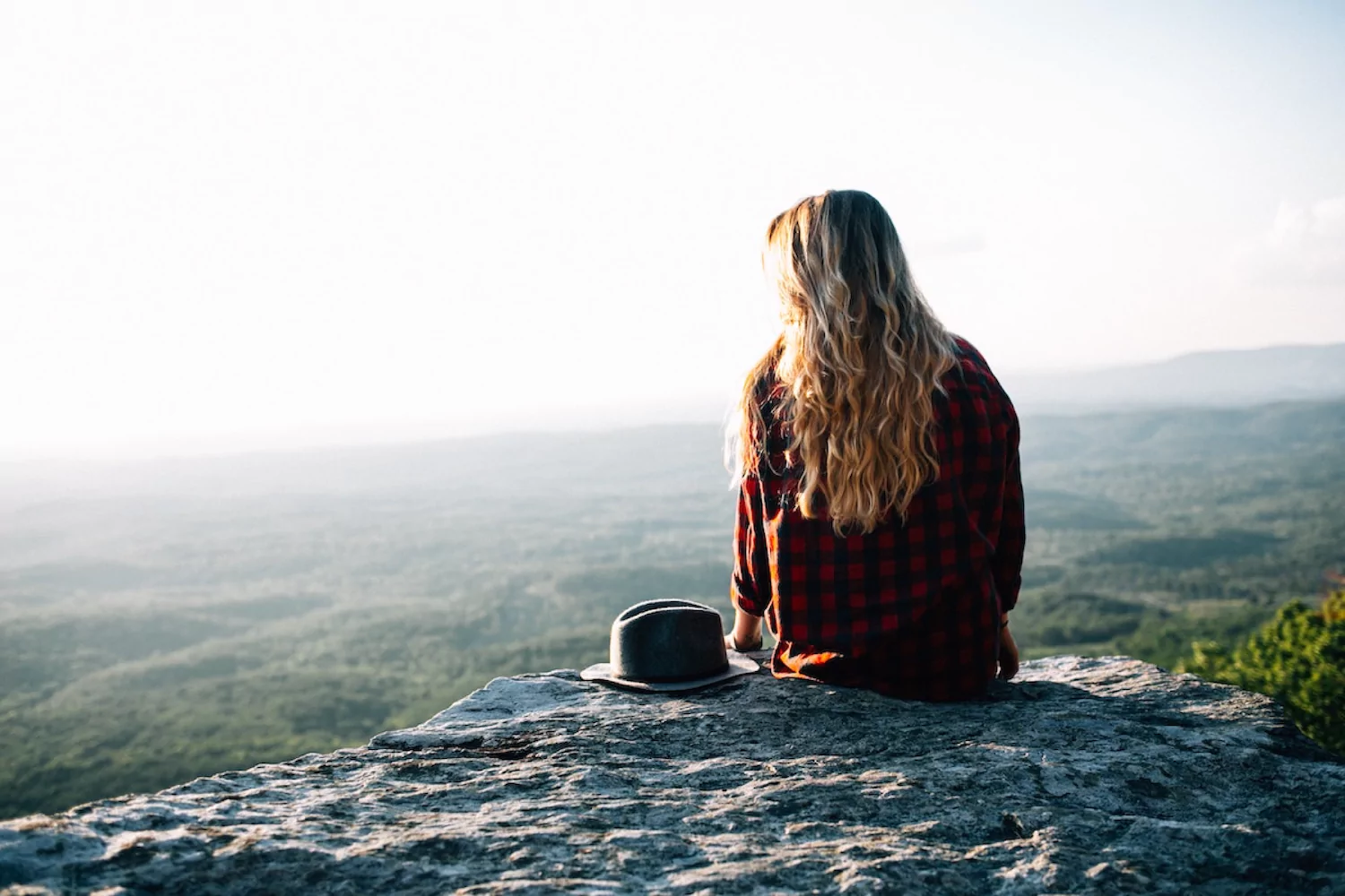 a pastor's wife sits at the edge of a cliff, looking out across treetops below