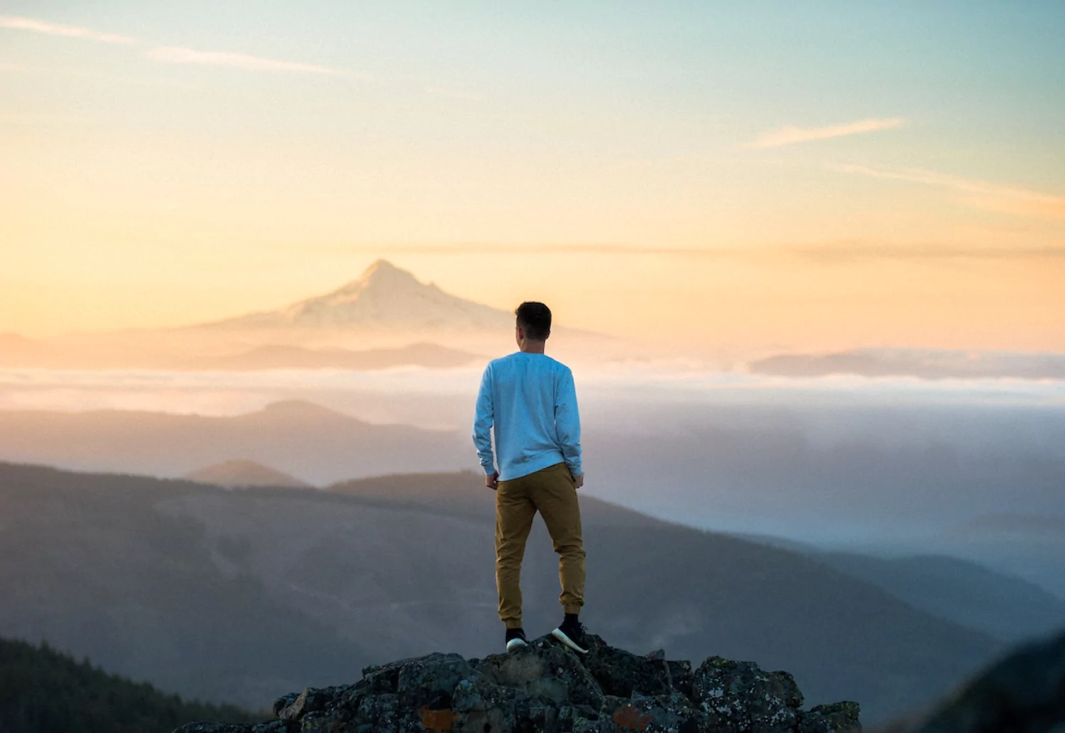 a young man stands on a rock overlooking mountain peaks at sunrise