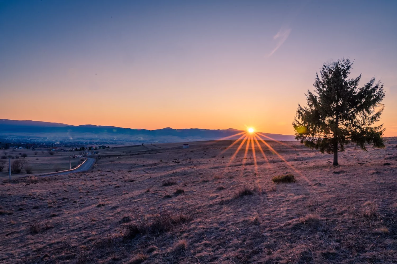 the sun setting behind mountains in a dry and grassy place