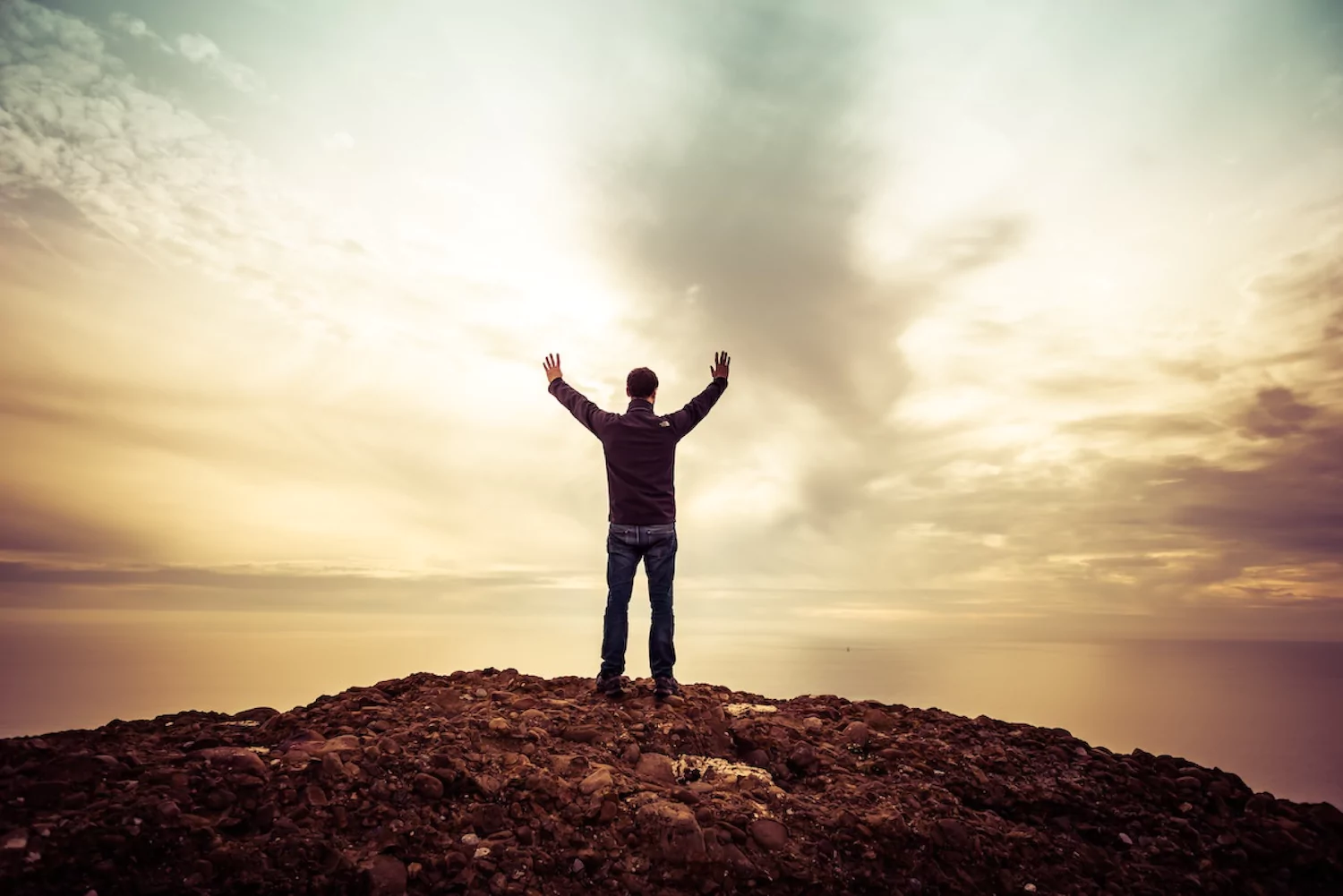 a pastor stands at the edge of cliff and looks out across a dim, cloudy horizon