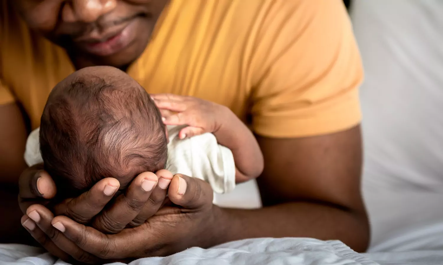 A close-up of a father cradling a newborn baby in his arms and looking upon the baby lovingly.