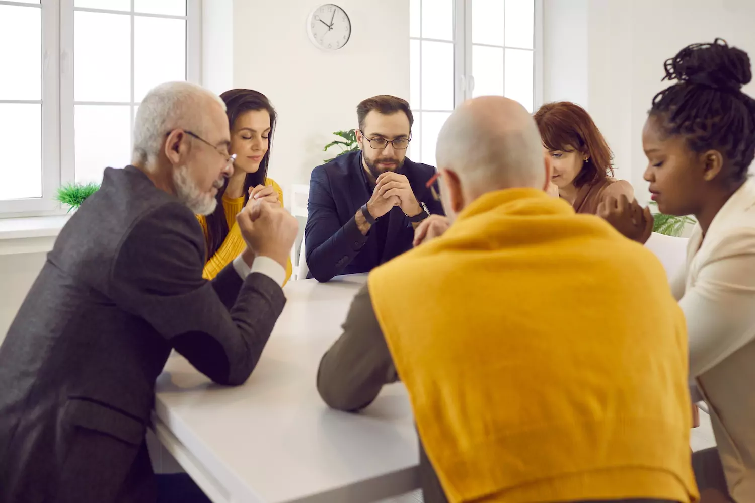 a group of church members sit around a table, praying together
