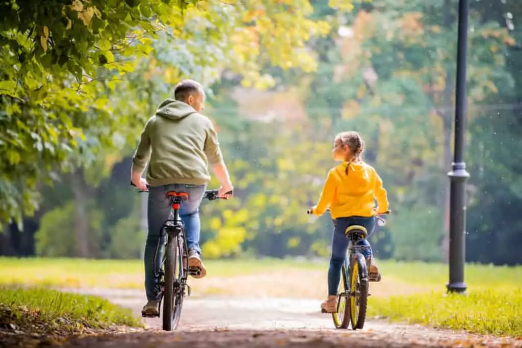 Happy father and daughter ride bicycles in the autumn park on a sunny day.