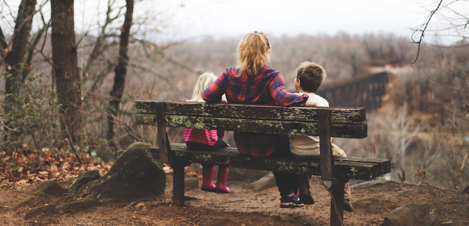 a pastor's wife sits with her two pastor's kids, a girl and a boy, on a park bench