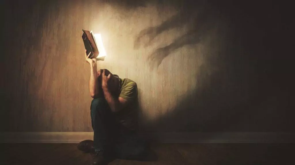 man holding Bible and hiding from spiritual warfare