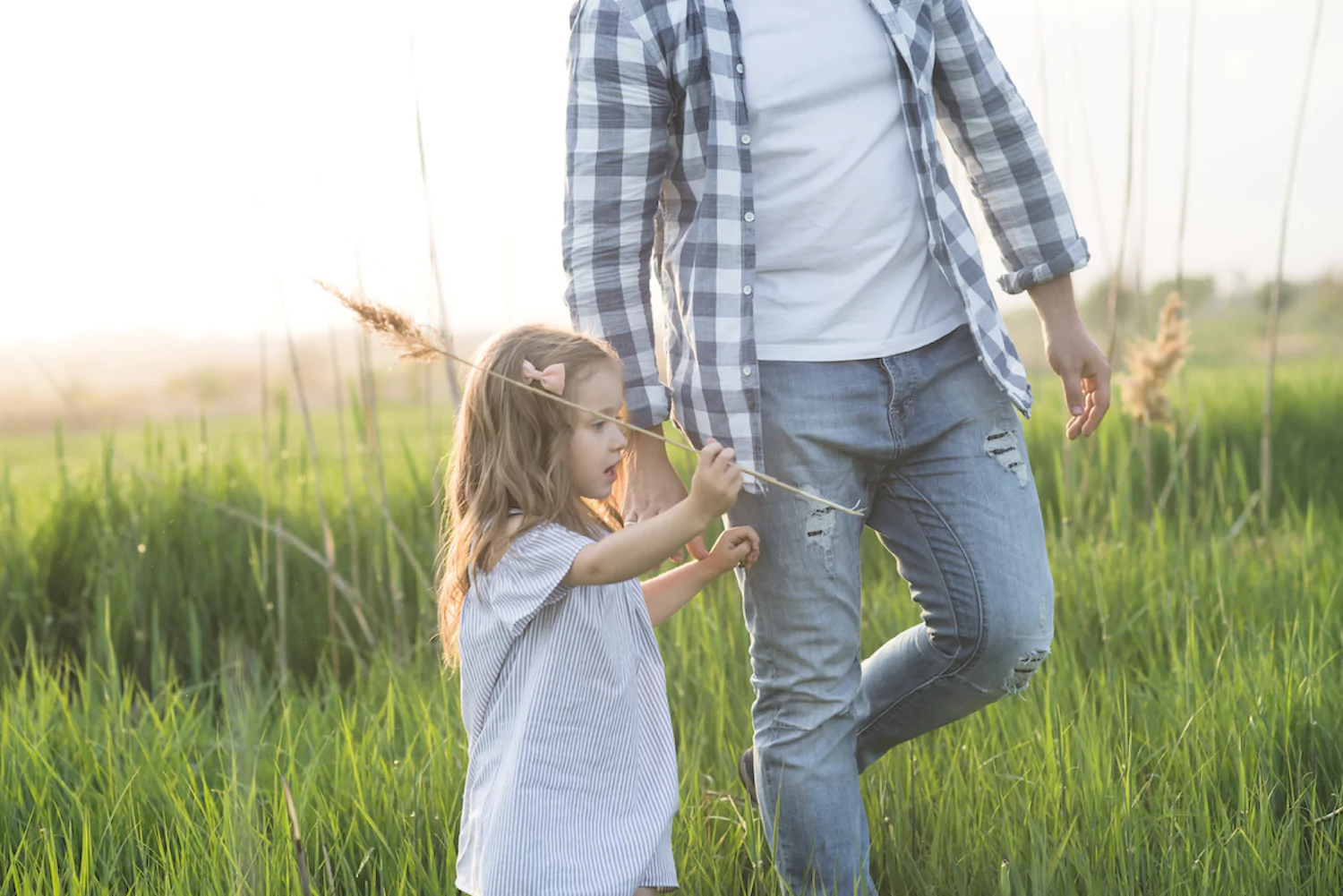 a pastor walks with his little girl in a field of tall grass