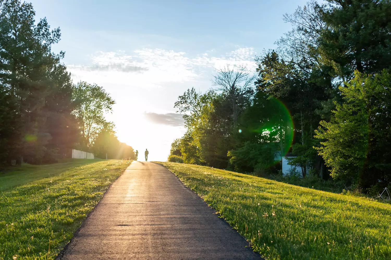 a pastor and his wife walk along a tree lined trail in the distance