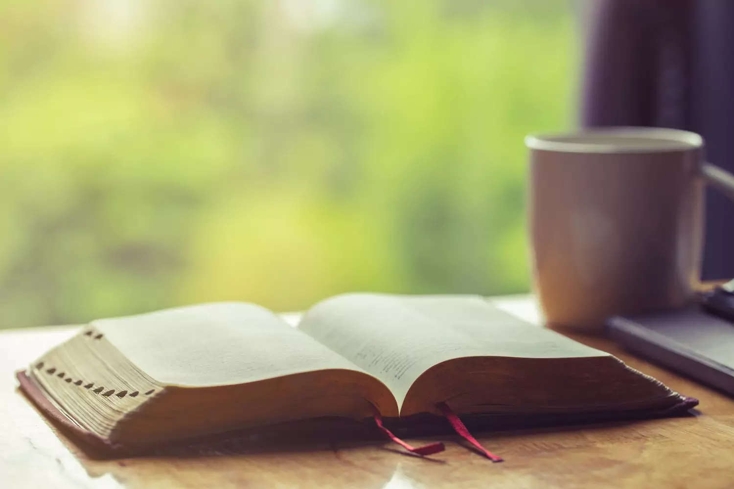 An pastor's open Bible and coffee mug sit on a table.
