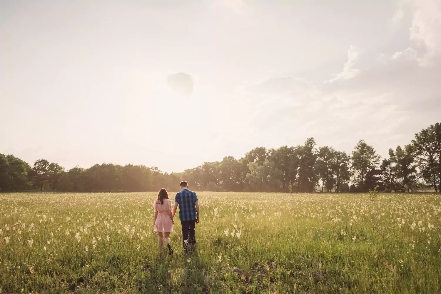 A pastor and his wife walk hand in hand through a field.