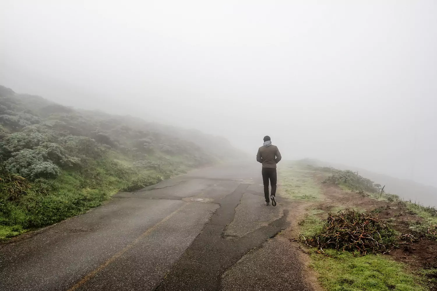 A man walks down foggy road.