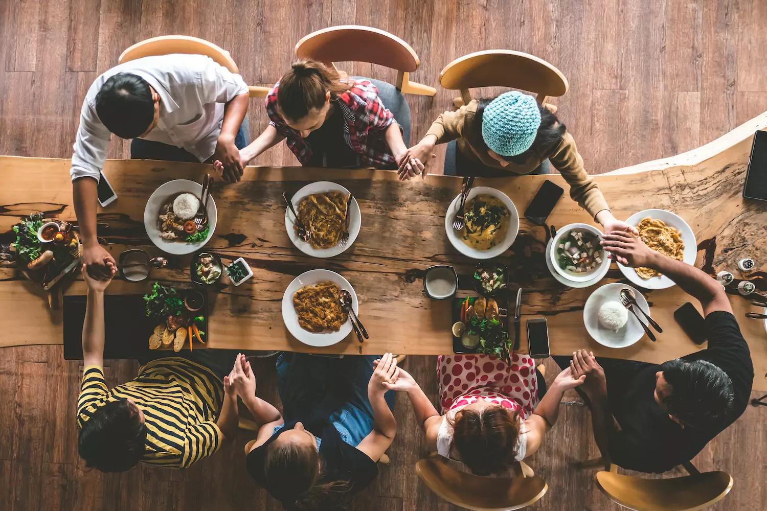 A family sits around the dinner table during a holiday gathering, holding hands to pray instead of fostering conflict.