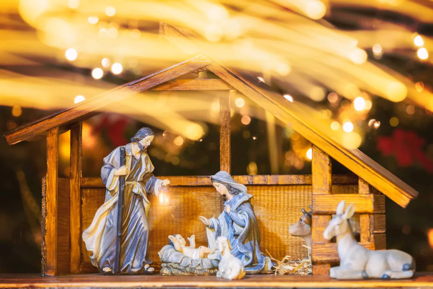 A nativity scene sits in front of glowing Christmas lights.