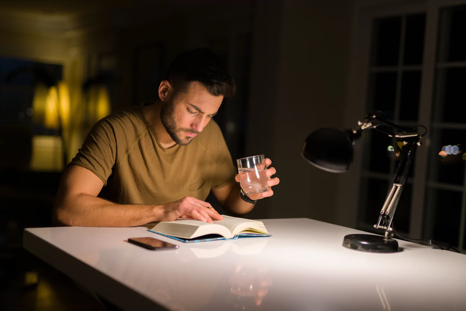 A pastor sits at a desk studying a book late at night.