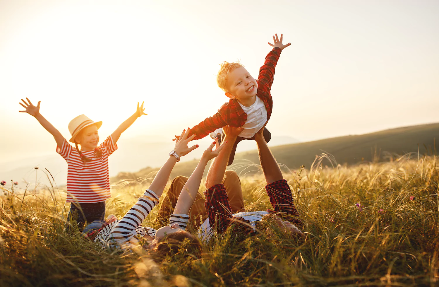 A family with foster children plays in a grassy field in golden light.