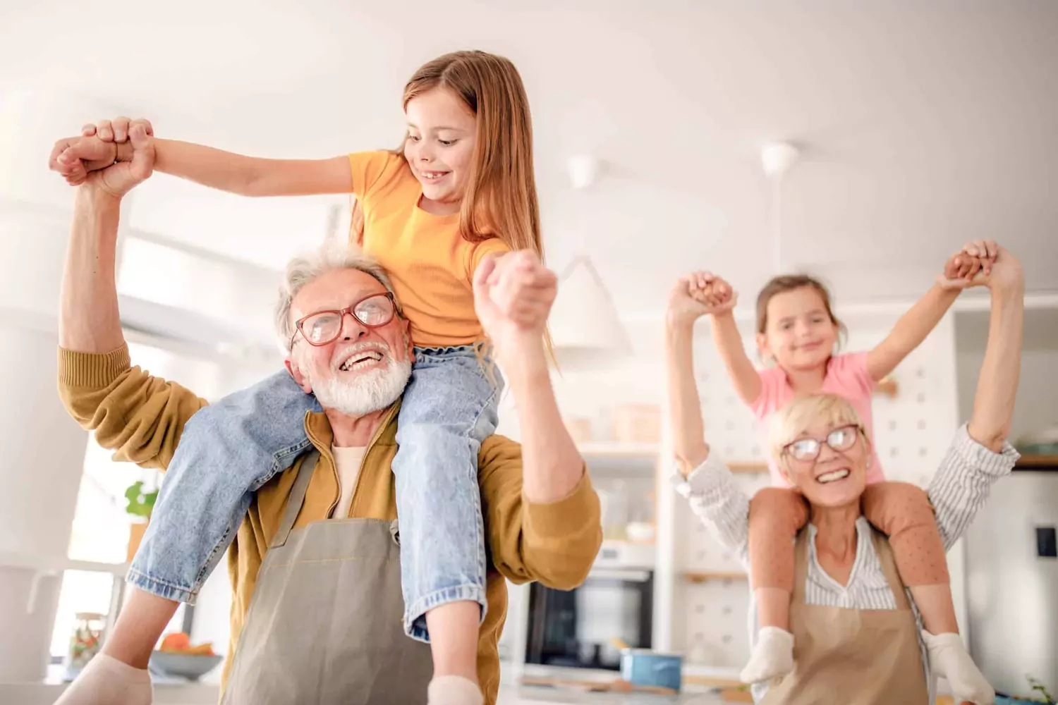 A grandfather and grandmother give their two granddaughters a piggy back ride through their house.