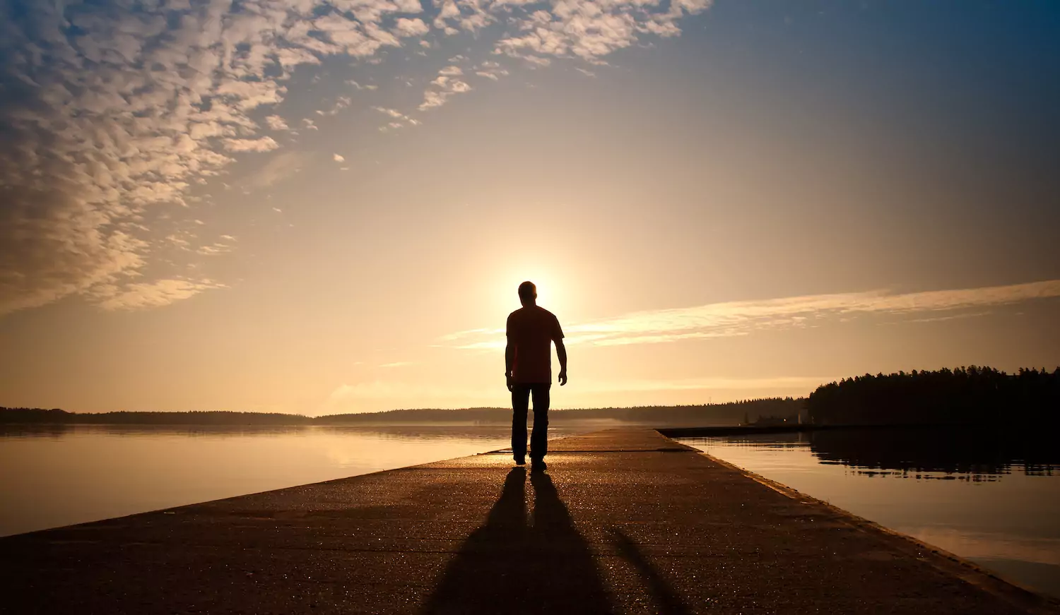 A pastor walks down a dock on the lake at dusk enjoying sabbath rest.