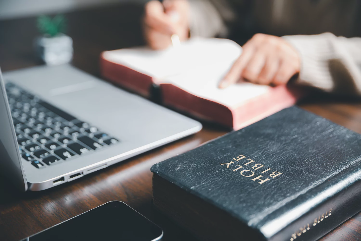 A pastor studies his Bible while sitting at his laptop to write a sermon.