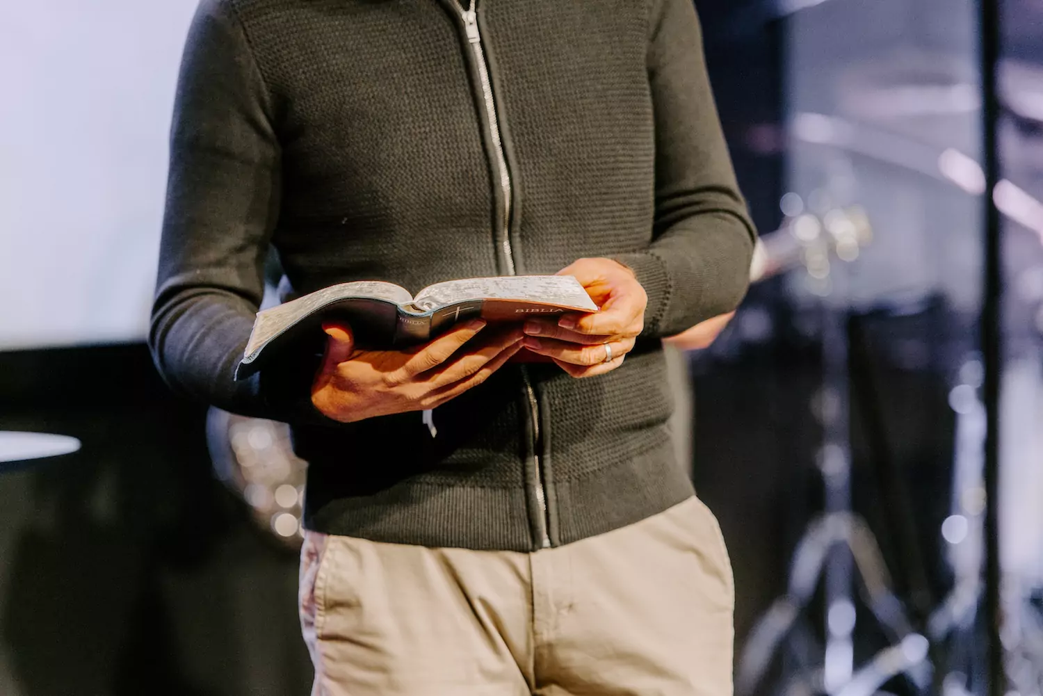 A pastor stands in front of the church holding his open Bible and preaching.