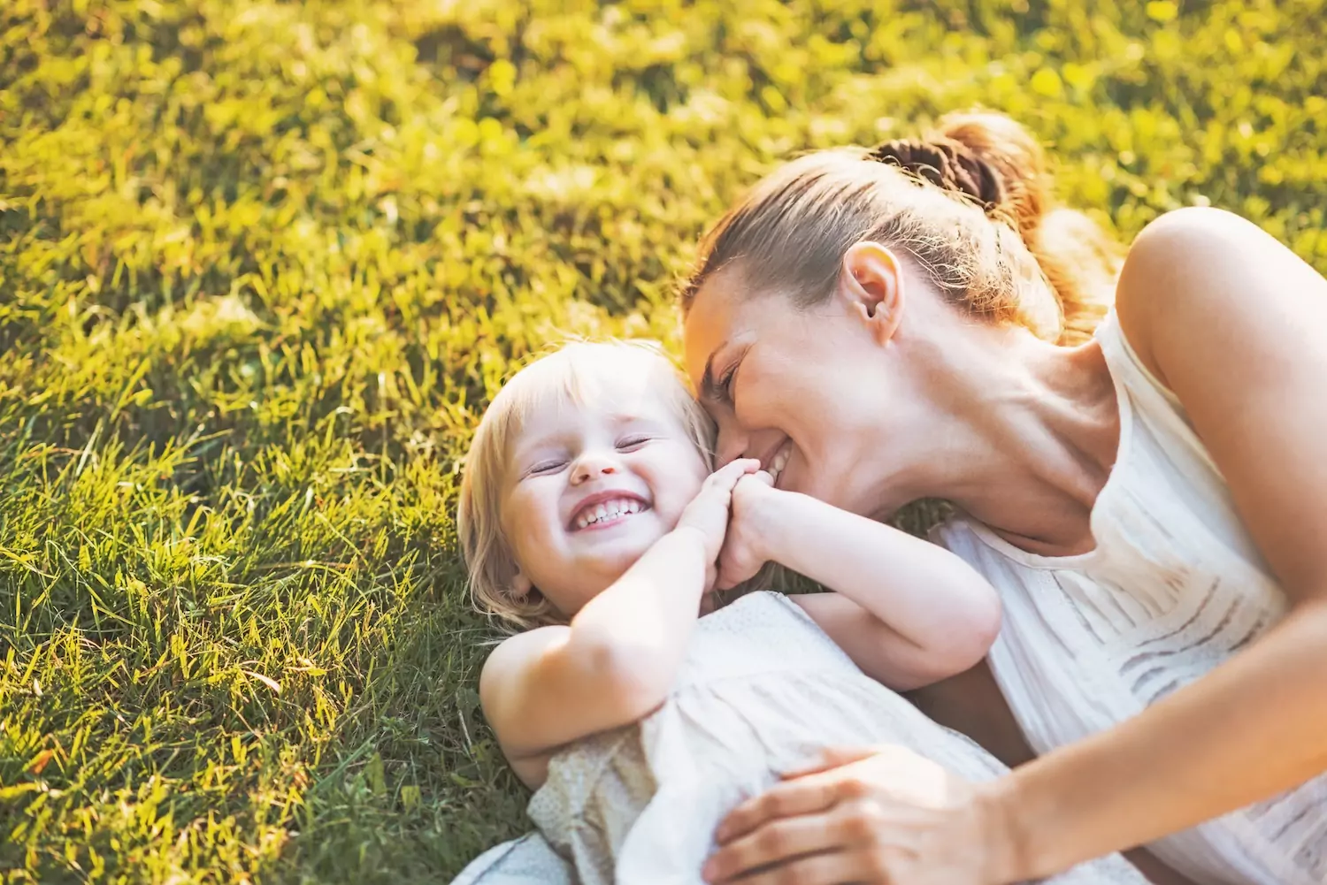 A pastor's wife snuggles her little girl in the grass as both laugh.