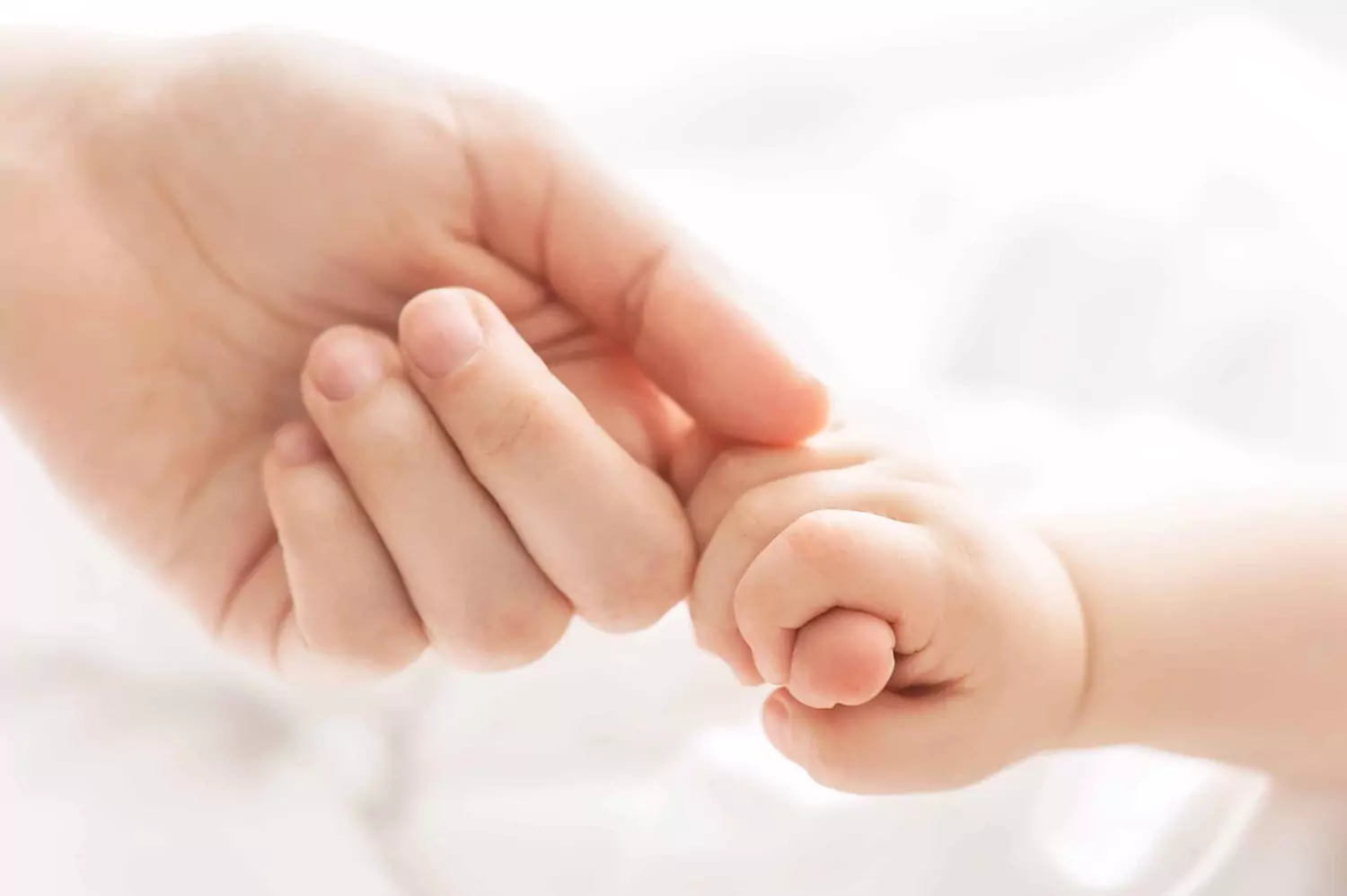 Close-up of a baby holding a woman's finger.