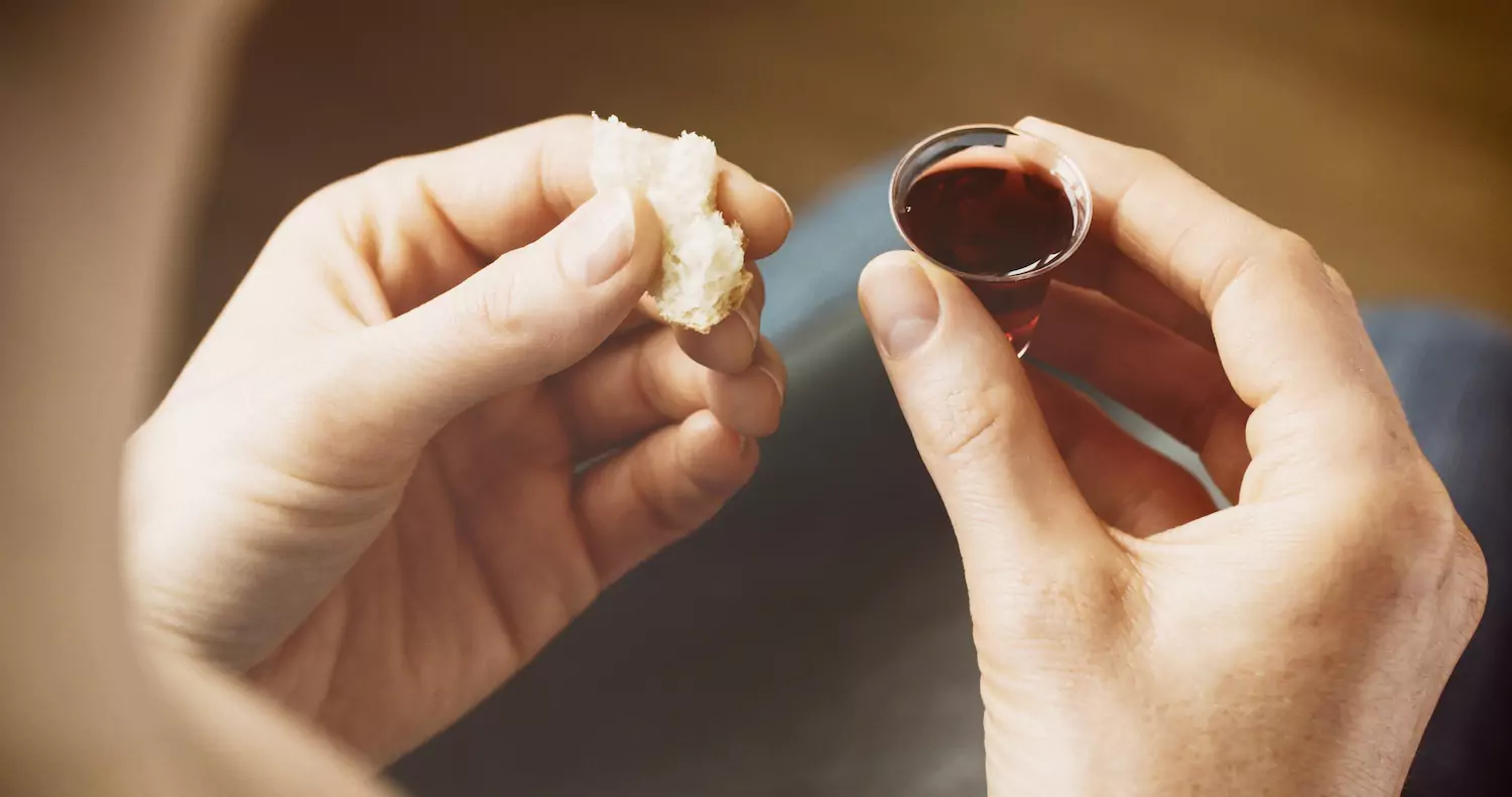 A man holds bread in one hand and juice in the other, preparing to partake in communion.