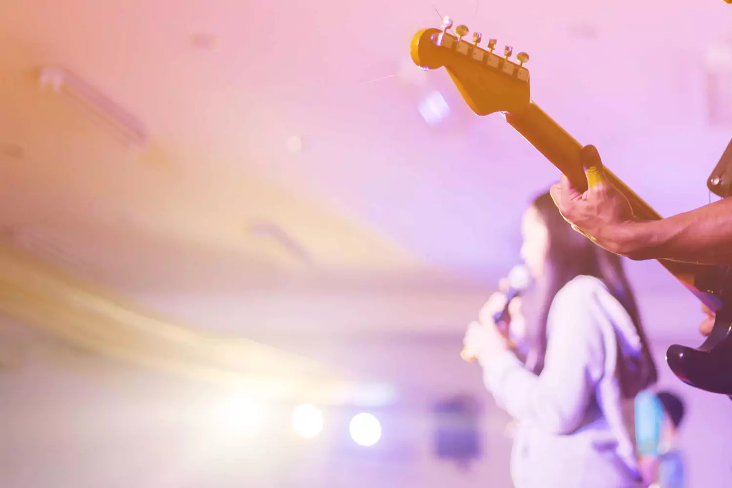 A worship guitarist and vocalist sing on stage while lights shine.
