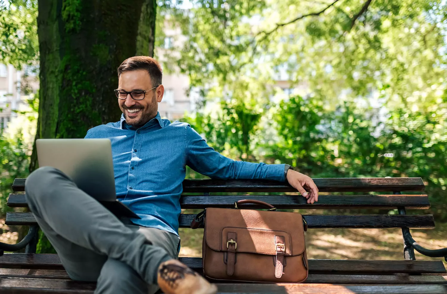 Pastor sits on a park bench smiling as he studies on his laptop.