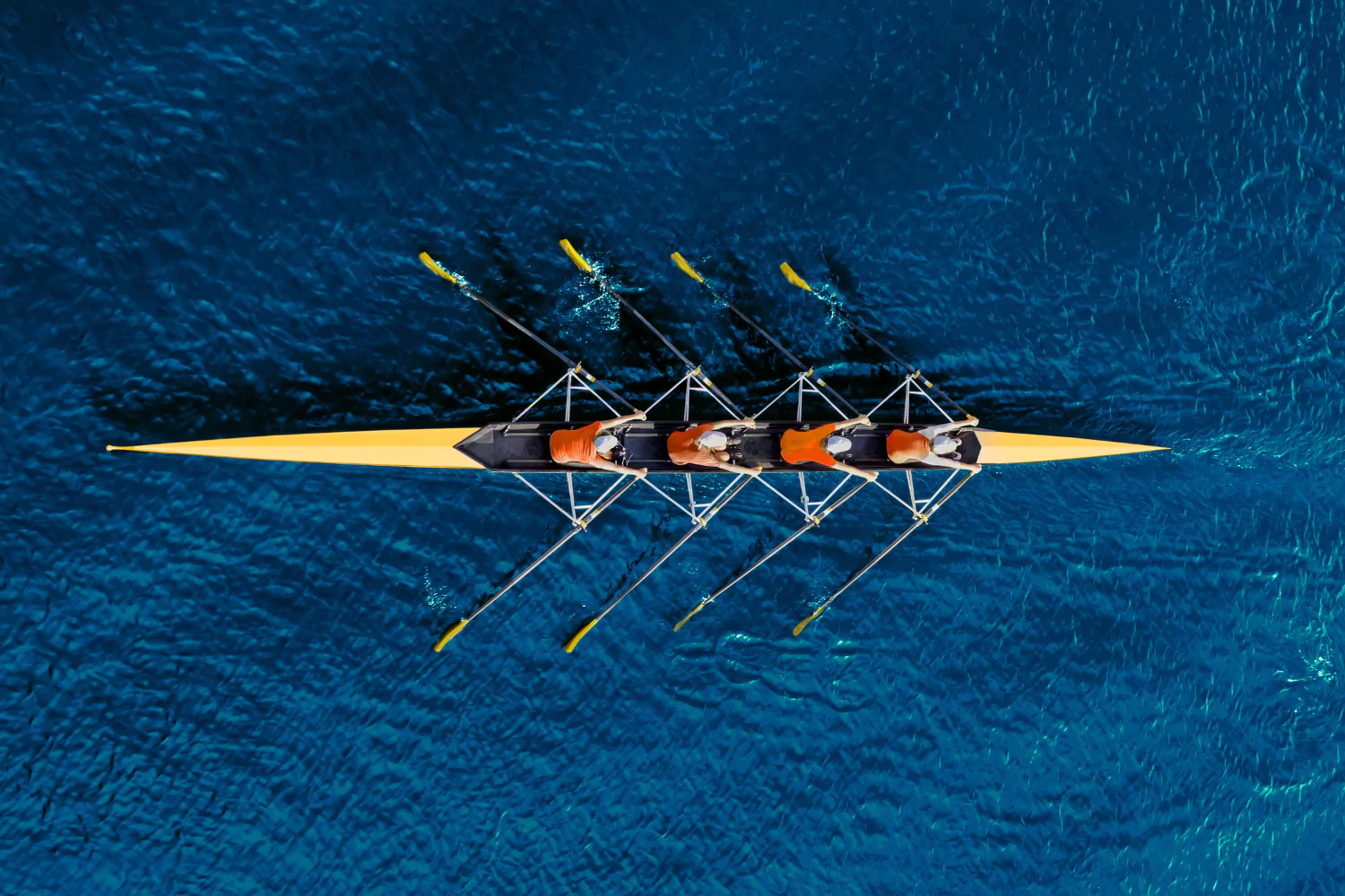 Aerial view of a rowing team in sync on deep blue water, symbolizing strong team leadership and coordination.