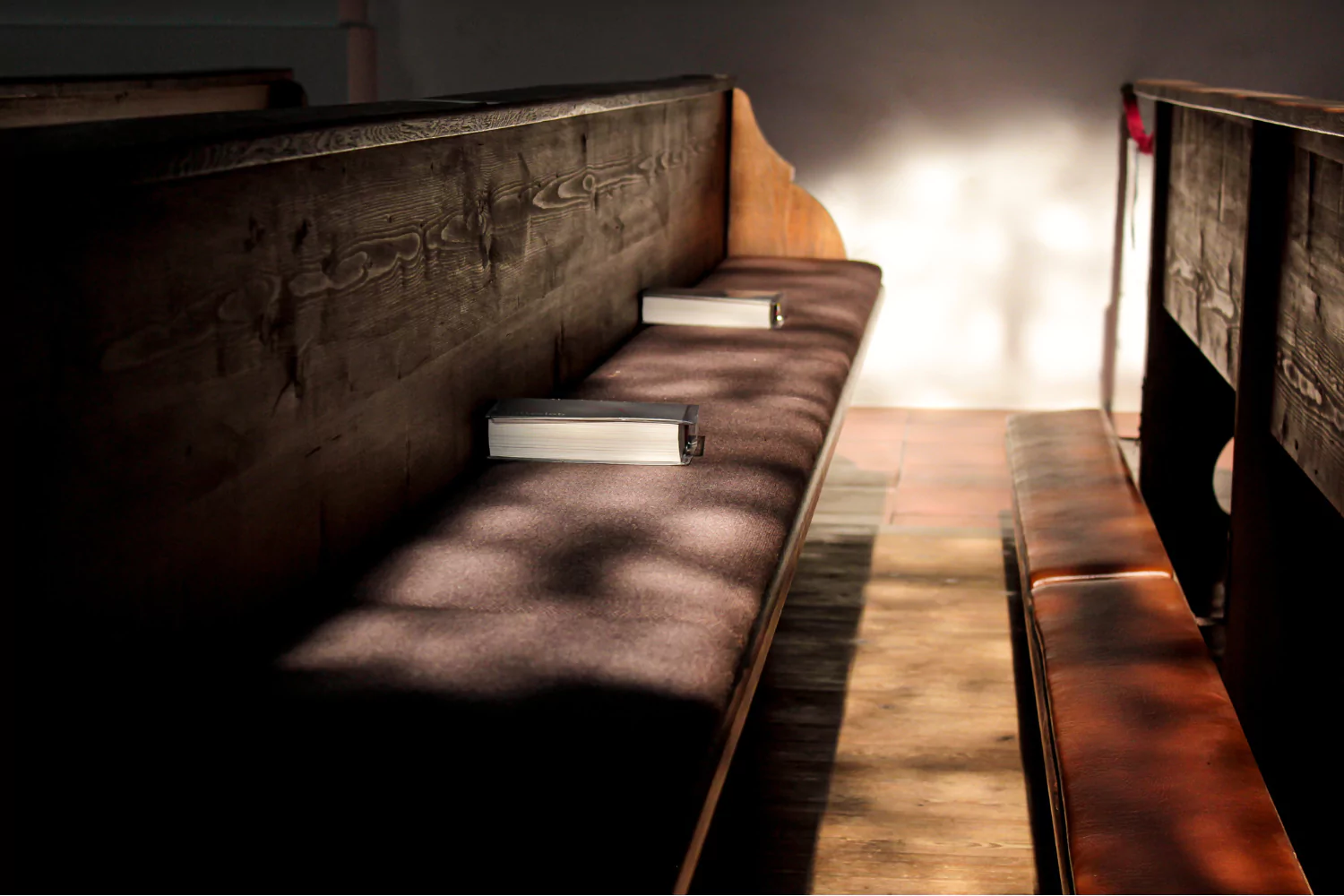Sunlight falls on empty wooden pews with closed hymnals, illustrating why churches die when congregations fade.
