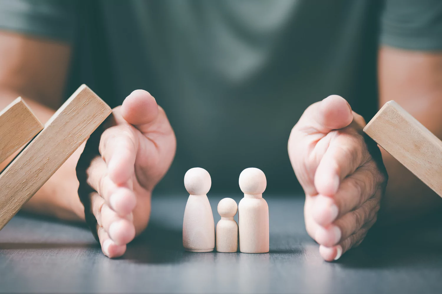 Hands shielding wooden figures of a family, symbolizing efforts to protect our children from harm.