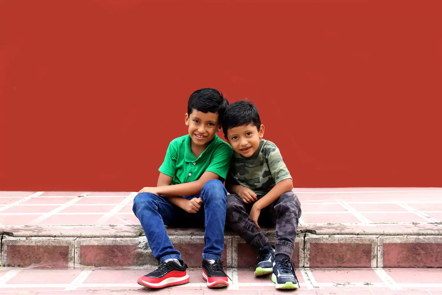 Two young boys sitting closely together on outdoor steps, smiling and illustrating the joy of biblical friendship.