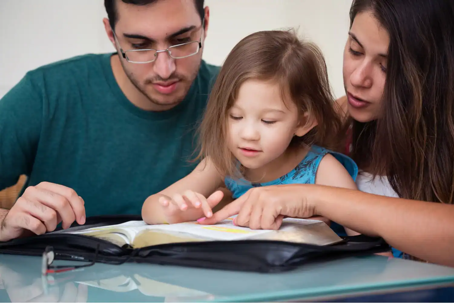 Parents guiding their young daughter through Scripture during family worship time.