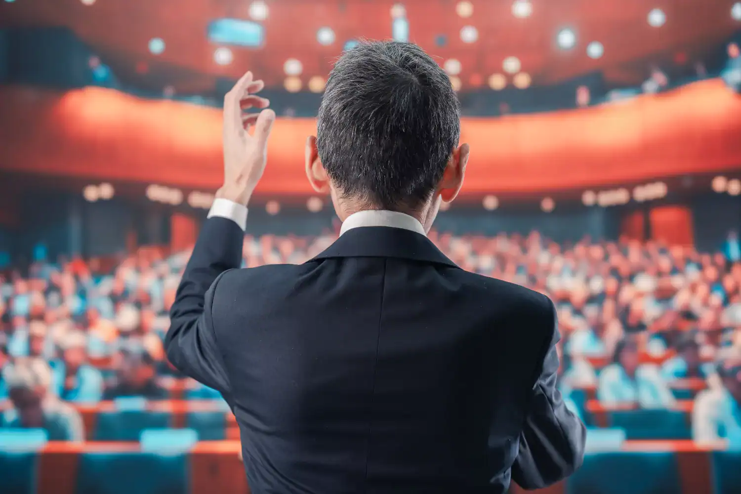 Man in a suit speaking to a large audience from a stage, symbolizing itinerant ministry, parachurch ministry, and the modern Christian platform.