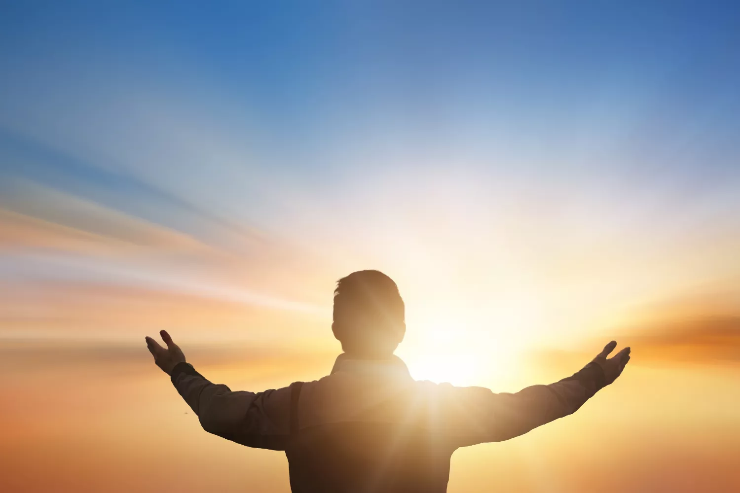A person stands with arms outstretched toward a bright sunrise, symbolizing gratitude and appreciation.